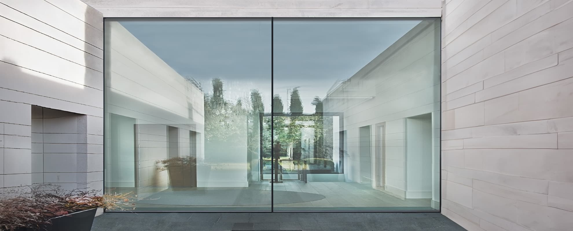 Coulissant minimal Cortizo COR Vision Plus en verre sans cadre dans un patio en pierre, reflets architecturaux