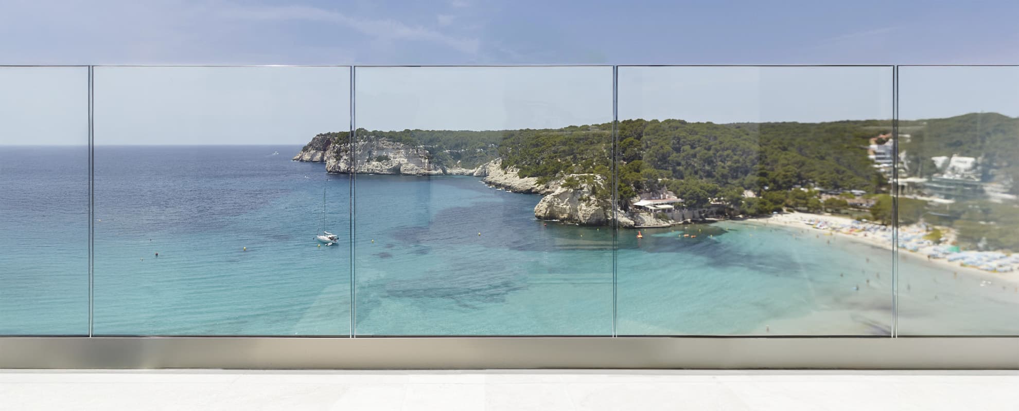 Garde-corps Cortizo View Crystal en verre sur une terrasse panoramique surplombant une crique méditerranéenne aux eaux turquoise