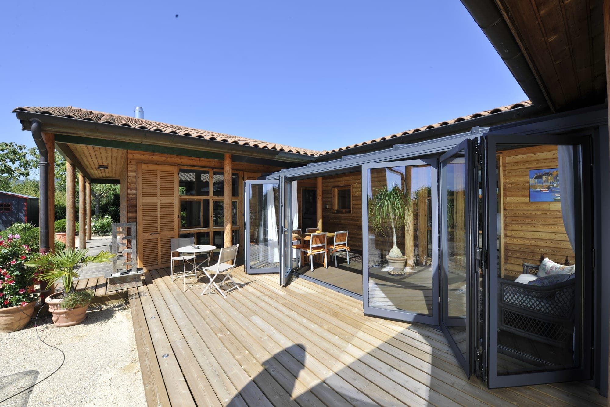 Reynaers CF 77 : porte repliable grise ouverte sur terrasse bois — maison de plage résidentielle bord de mer
